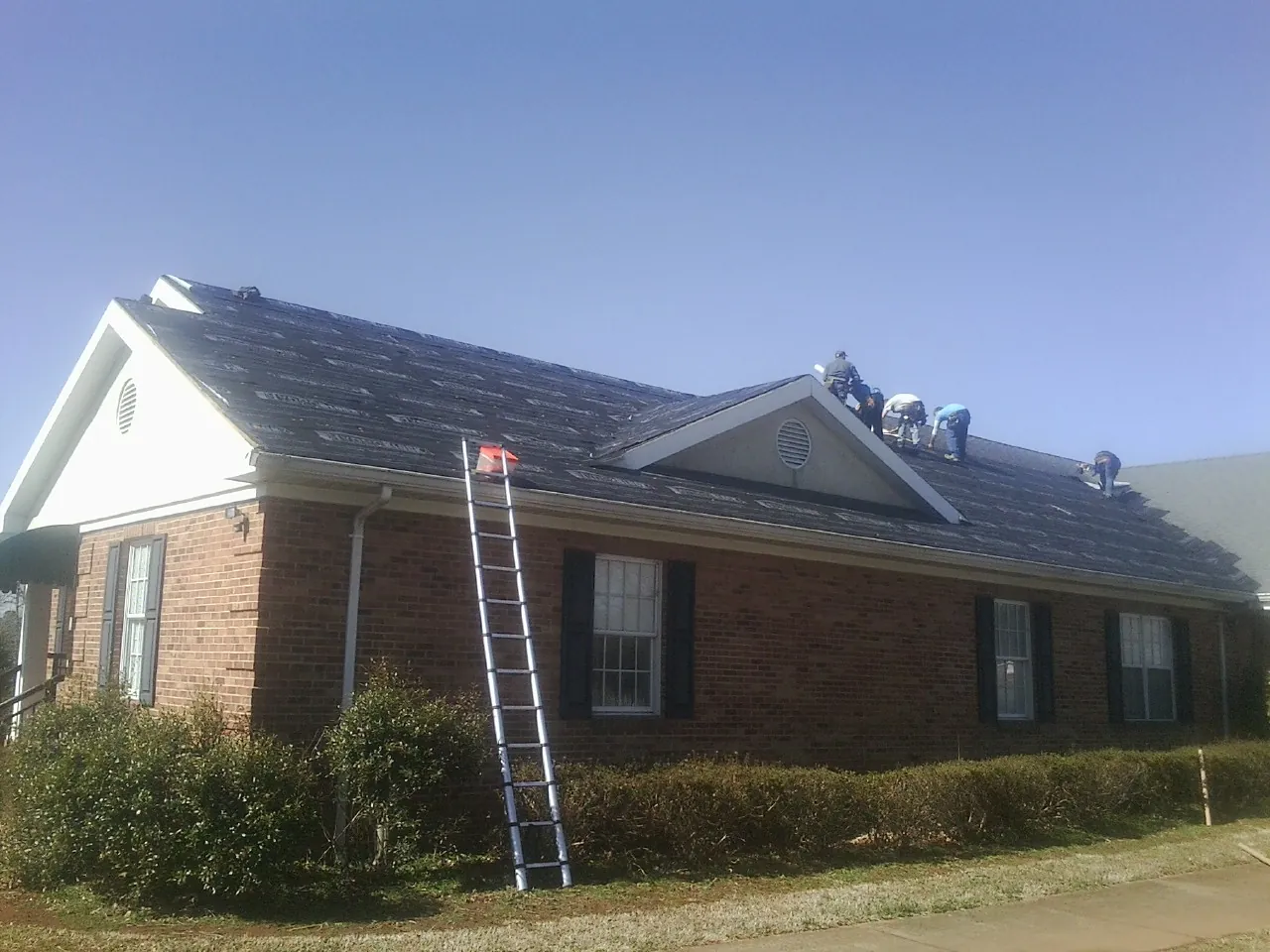 Crew tearing shingles off a brick ranch roof with a ladder set — Metal Roof Repair work by our crew in Pleasant Grove